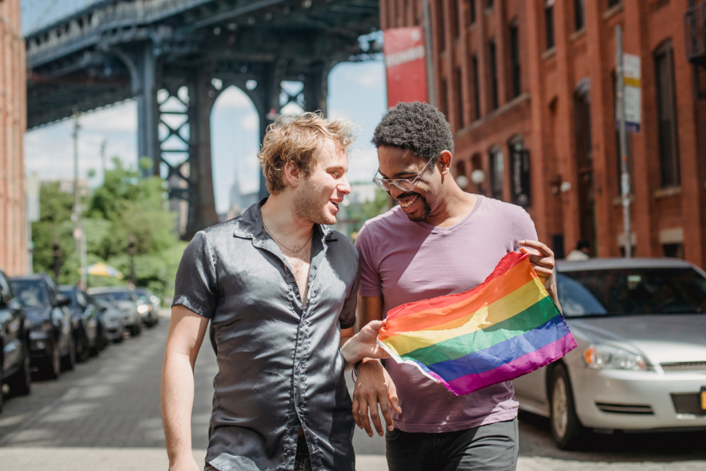 Two men smiling as they carry a Pride flag.